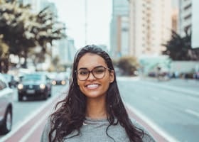 A young woman with glasses smiling on a city street, embracing urban lifestyle.