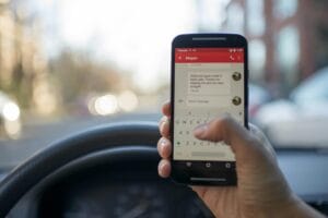 Close-up of a person texting on a smartphone while driving a vehicle, highlighting distracted driving.