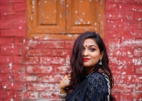 Charming woman in traditional attire posing against a rustic brick wall, showcasing elegance and cultural heritage.