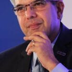 Portrait of a thoughtful businessman in a suit, wearing eyeglasses, captured in an indoor corporate setting.