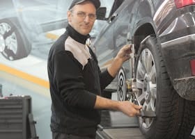 Mechanic performing wheel alignment on a car in a professional garage setting.