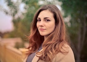 A young woman with long hair smiles confidently for an outdoor portrait session.