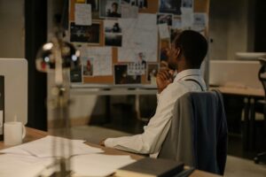 Detective in thought examining evidence board in a dimly lit office environment.