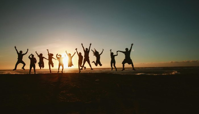 Silhouette of a group of friends jumping on a beach at sunset, expressing joy and freedom.