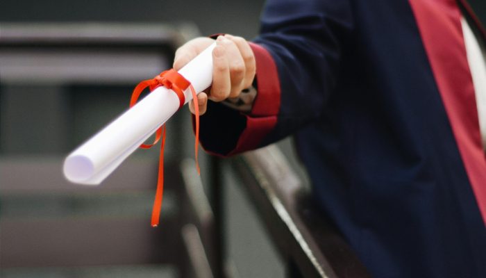 A close-up image of a graduate holding a diploma tied with a red ribbon, symbolizing achievement and success.