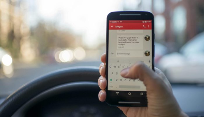 Close-up of a person texting on a smartphone while driving a vehicle, highlighting distracted driving.